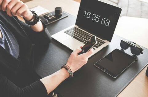 woman using a smartphone while fronting a macbook pro and black ipad